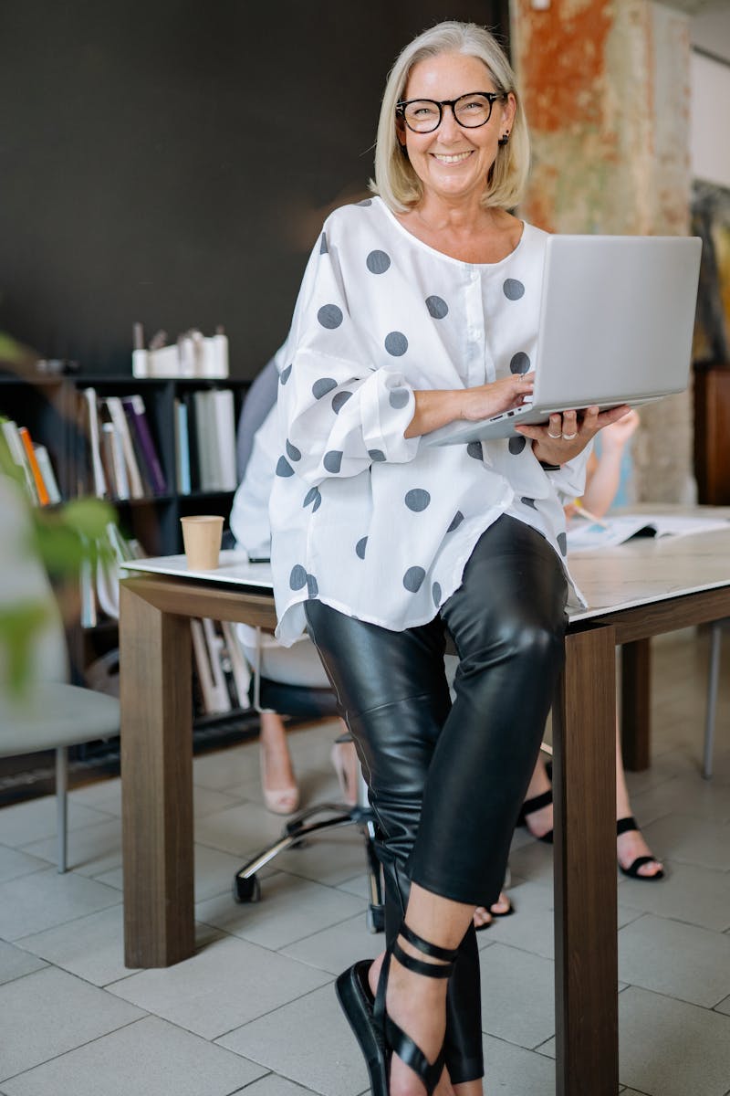 Senior woman wearing glasses, smiling while holding a laptop.