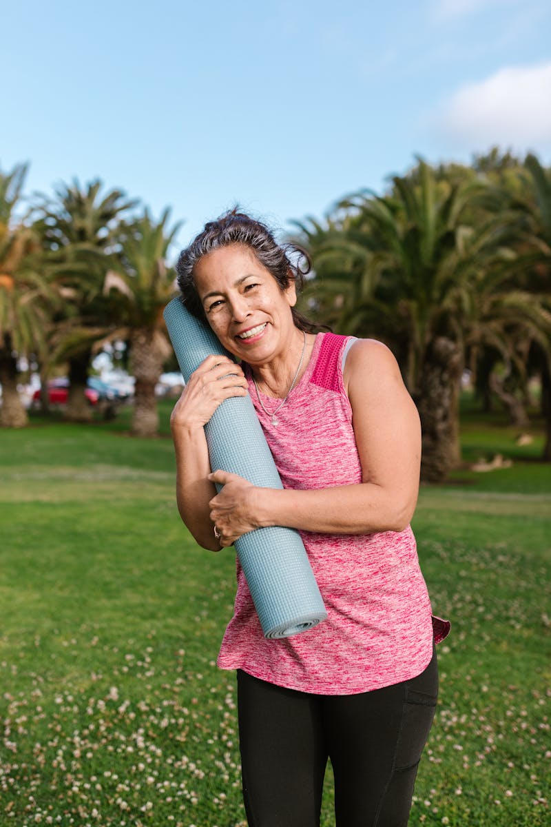 Senior woman in activewear holding a yoga mat outdoors, promoting wellness and fitness.